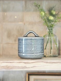 a blue pot sitting on top of a counter next to a vase filled with flowers