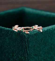 a close up of a ring with green stones on the side and leaves in the middle