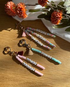 four keychains with beads and tassels are on a table next to flowers