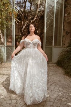 a woman in a white wedding dress standing on a brick walkway with her arms behind her back