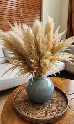 a blue vase with dry grass in it on top of a wooden table next to a couch