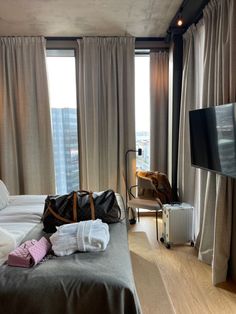 a hotel room with a bed, luggage bag and television in front of large windows