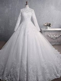 a white wedding dress with long sleeves and lace on the skirt is displayed in front of a