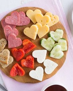 a wooden plate topped with heart shaped cheeses and crackers next to a cup of coffee