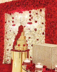 a wedding cake surrounded by red roses and candles on a table in front of a floral wall