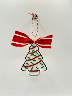 a christmas tree ornament hanging from a red and white ribbon on a wall