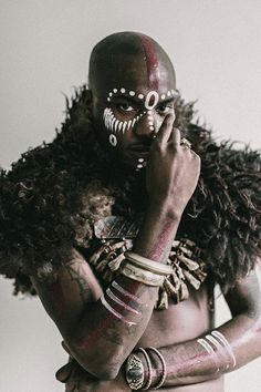 a man with tattoos and piercings on his face talking on a cell phone while standing in front of a white wall