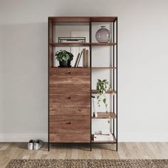 a book shelf with books and plants on it in an empty room, next to a rug