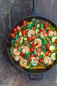 a skillet filled with shrimp, tomatoes and zucchini on top of a wooden table