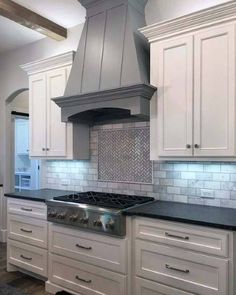 a kitchen with white cabinets and gray counter tops, an oven hood over the stove