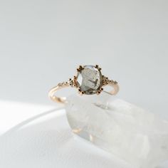 a white diamond ring sitting on top of a piece of clear quartzite with gold accents