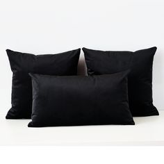 three black pillows sitting next to each other on a white surface with one pillow in the middle