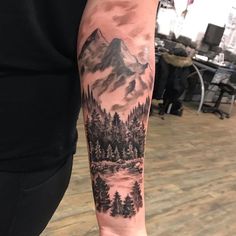 a man's arm with a mountain and trees tattoo on the left side of his arm