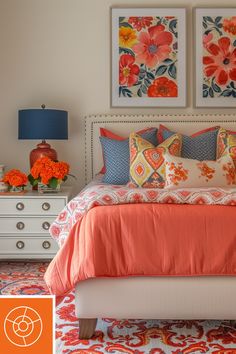 a bed with orange and blue pillows in a bedroom next to two pictures on the wall