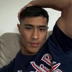 a young man sitting on a couch with his arm behind his head and looking at the camera