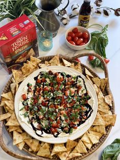 a platter filled with tortilla chips, tomatoes and olives next to a bottle of wine