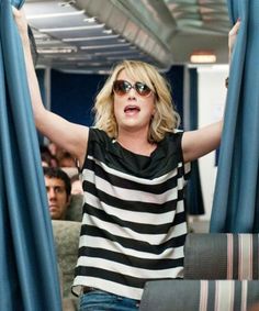 a woman with her arms in the air while riding on a train, wearing sunglasses