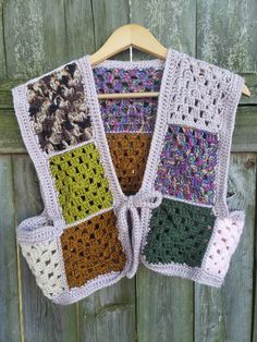 a multicolored crocheted sweater hanging on a wooden fence