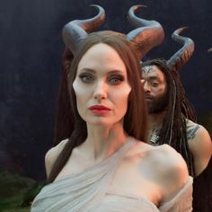 a woman with horns on her head standing next to a man in a white dress