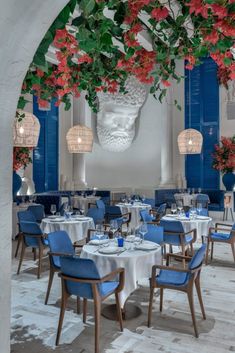 a dining room with blue chairs and white tablecloths covered in red flowers hanging from the ceiling