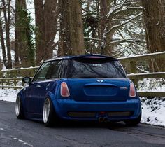 a small blue car parked on the side of a road in front of some trees