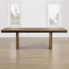 a wooden table sitting on top of a hard wood floor next to two large windows