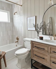 a white toilet sitting next to a bath tub in a bathroom under a large mirror