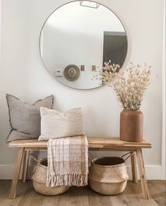 a wooden table topped with pillows next to a round mirror and vase filled with flowers