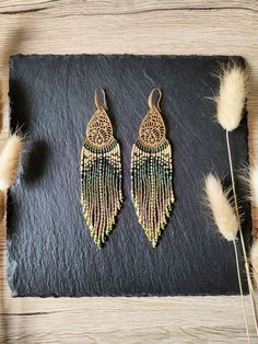 two pairs of earrings sitting on top of a black slate slab next to some dry grass