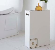 a white toilet sitting next to a trash can with a plant on top of it