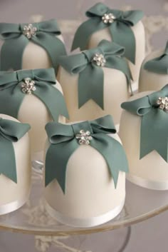 small white cakes with green bows on them sitting on a glass cake platter,