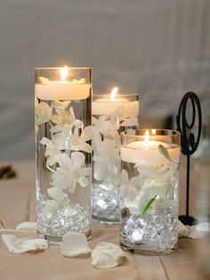 three glass vases filled with white flowers and lit candles