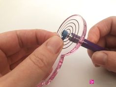 two hands are holding a purple pen and drawing on a piece of glass with pink liquid