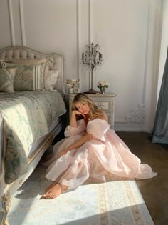 a woman in a pink dress sitting on the floor next to a bed and reading a book