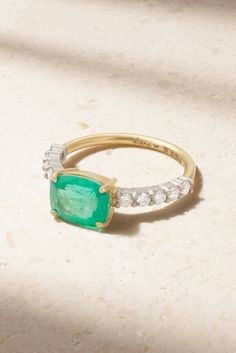 an emerald and diamond ring sits on a marble surface