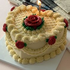 a cake with white frosting and red roses on it is sitting on a table