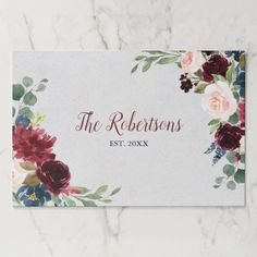 an elegant floral wedding place card with burgundy, pink and green flowers on white marble