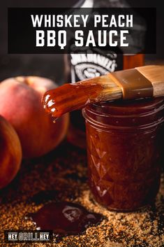 a bottle of whiskey peach bbq sauce next to two peaches and a brush