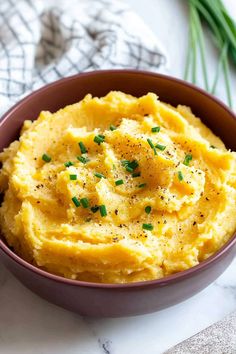 a bowl filled with mashed potatoes on top of a white countertop next to green onions