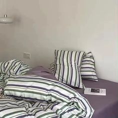 a bed with striped sheets and pillows on top of it next to a wall lamp