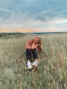 a woman sitting in the middle of a field with her head on her hands and eyes closed