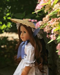 a doll with long hair wearing a straw hat and blue dress sitting on a bench