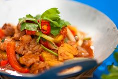 a white bowl filled with meat and vegetables on top of a blue tablecloth covered table