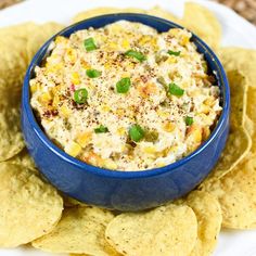 a bowl of dip surrounded by tortilla chips on a white and blue plate