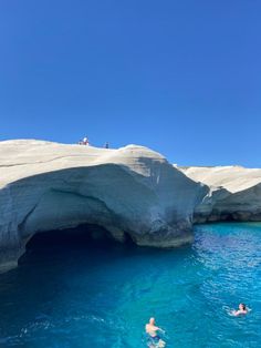 two people swimming in the blue water near an ice cave