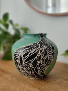 a green vase sitting on top of a wooden table next to a potted plant