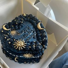 there is a blue cake with gold decorations on the top and sides in a box