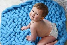 a baby in a diaper is sitting on a blue crocheted blanket and smiling at the camera