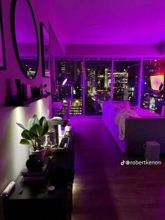 a living room filled with furniture and purple lighting in front of a large window overlooking the city