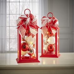 two red and white christmas ornaments in a lantern style holder on a counter top with a window behind them